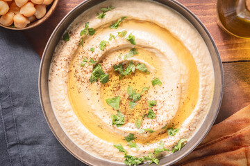 Arabic cuisine; Traditional creamy hummus dip in dark bowl. Topped with olive oil, paprika and parsley. Top view with close up.