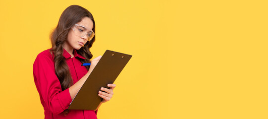 concentrated teenager girl in protective glasses making notes in folder with documents. Child builder with protective glasses horizontal poster design. Banner header, copy space.