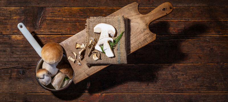 Dark food photography background - Forest mushrooms / Boletus edulis (king bolete) / penny bun / cep / porcini / mushroom and fern on old wooden cutting board on table