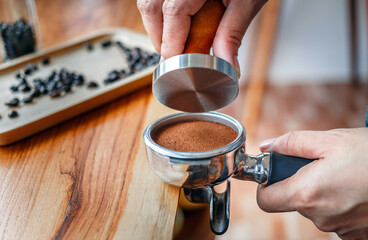 Close-up of hand Barista cafe making coffee with manual presses ground coffee using tamper on the wooden counter bar at the coffee shop