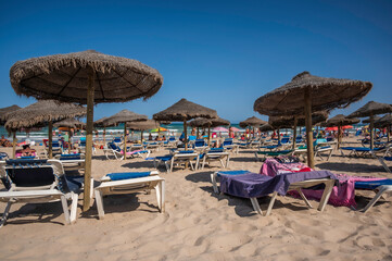 A Spanish beach in the summer, with rows of sun loungers and shades along the sand