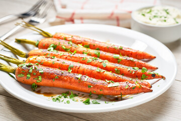 Roasted carrot with sauce in a bowl on a white wooden table. Caramelized Carrots. Close-up.