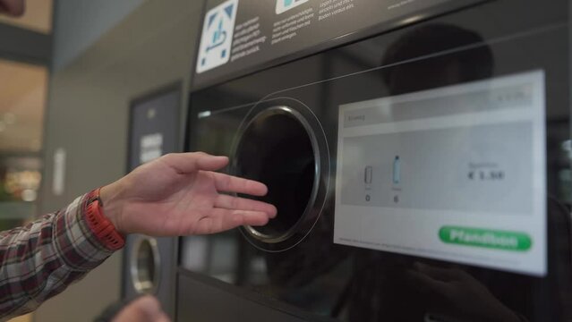 Male returns plastic bottles, reusable containers to reverse vending machine in Munich, Germany supermarket. Man using bottle deposit point. Automatic bottle recycling machine for collection plastic. 