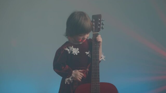 Cute little girl stands on stage in vintage dress and plays an acoustic guitar like a counter bass or cello. The concept of performing the author jazz and blues music. Hobbies and art among children