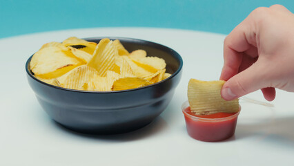 cropped view of man dipping ridged potato chips in ketchup on blue.