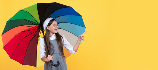 happy school girl in glasses. teen child under colorful parasol pointing finegr. Child with autumn umbrella, rainy weather, horizontal poster, banner with copy space.