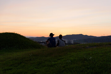 Fototapeta na wymiar Lovely Couple sitting on the green hill to enjoy sunset
