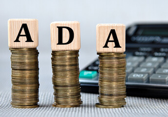 ADA - acronym on wooden cubes on the background of coins and calculator