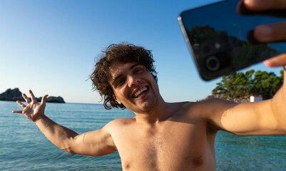 Smiling young man taking selfie at the beach with the sea at the background.