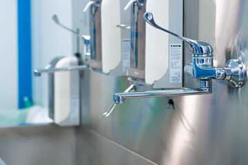 Selective focus on a shiny faucet of a sterile steel washbasin in a modern operating room. Hand...