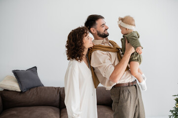 cheerful young father holding in arms infant daughter near curly wife.