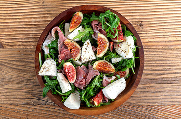 Salad with arugula , figs, prosciutto and mozzarella on wooden background