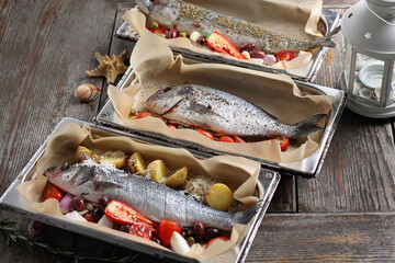 Sea bass, sea bream and mackerel in baking dishes, on table. Baking fish with vegetables in sheet...