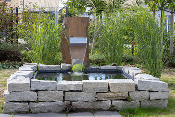 Urban garden with a square high pond and a small waterfall created by a stainless steel outlet...