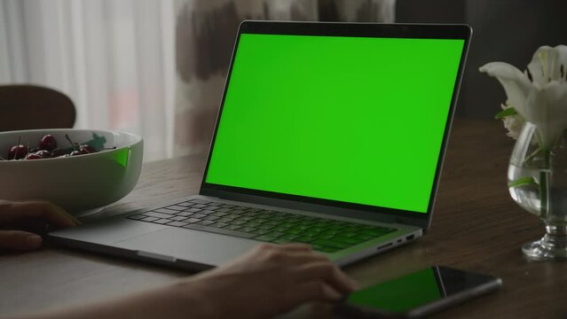 Handheld shot pivoting around laptop computer with chroma key green screen and woman hands