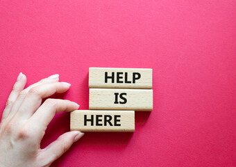 Help is here symbol. Wooden blocks with words Help is here. Beautiful red background. Businessman hand. Business and Help is here concept. Copy space.