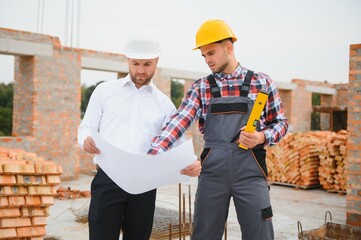 engineer and builder in hard hats discussing blueprint on construction site.