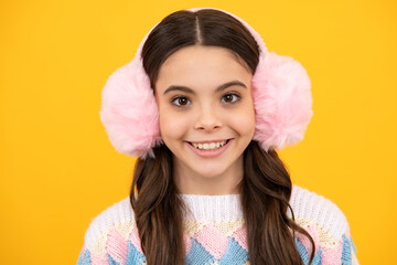 Beautiful teen girl in a winter warm earmuff ear-flaps hat and a warm sweater. A child on a yellow isolated background.