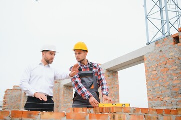 Construction engineers supervising progress of construction project stand on new concrete floor top roof and crane background.