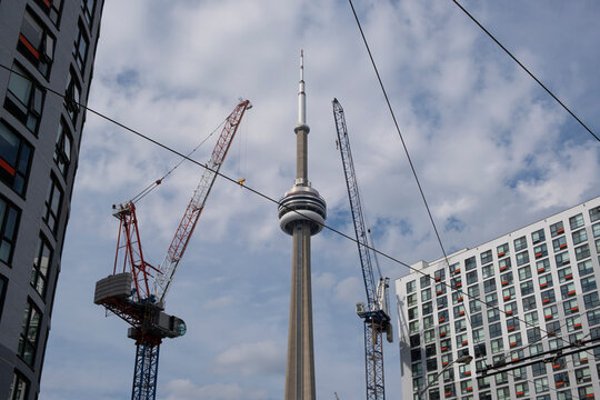 CN Tower main pod surrounded by construction cranes and residential buildings, shot against blue sky. New real estate developments concept.