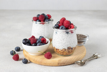 Chia pudding with muesli, fresh berries and natural yogurt on a wooden board on light gray table. Healthy breakfast concept
