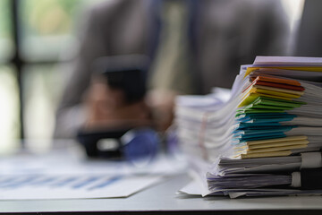 Businessman working in finance with pile of unfinished papers on the desk business paper pile
