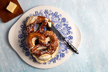 German Brezel pretzel with butter on a plate with white blue patterns on a blue background. Served with a slice of butter for breakfast.