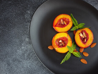 Summer dessert - Cooking Ripe grilled peaches with honey and nuts over dark plate and table. Selective focus with blurred foreground and background. closeup