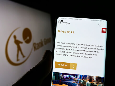Stuttgart, Germany - 09-15-2022: Person holding smartphone with webpage of British gambling company The Rank Group plc on screen in front of logo. Focus on center of phone display.