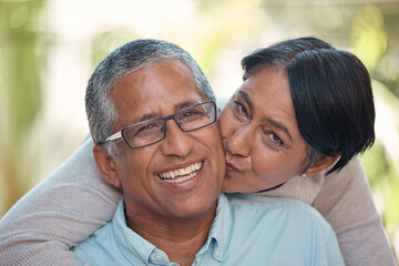 Love, kiss and happy senior couple sharing commitment, hug and affection while sitting together showing smile. Portrait of elderly indian man and woman enjoying retirement and free time to bond