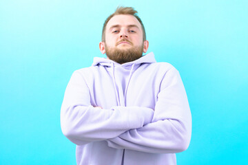 A suspicious man with crossed arms looks from the top on a blue background. Person. Standing. Man. Portrait. Adult. Arm. Crossed. Male. Happy. Studio. Confidence. Confident. Guy. Smile