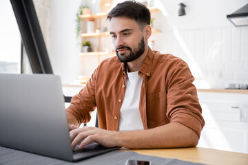 Obraz premium bearded freelancer using laptop while working from home near smartphone on table.