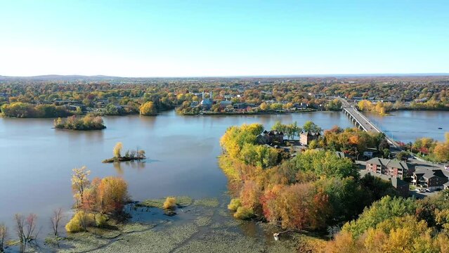 Aerial drone video moving backward revealing the city of St-Eustache, the Arthur-Sauve bridge accross the Mille Iles river with the colorfull trees of Autumn