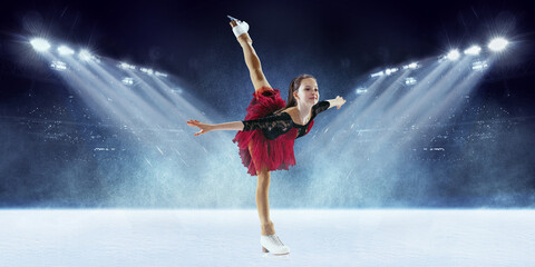 Beautiful female beginner figure skater in stage dress skating at ice arena with spotlights. Dance,...
