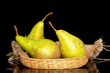 Three juicy organic pears on a straw dish, macro, isolated on a black background.