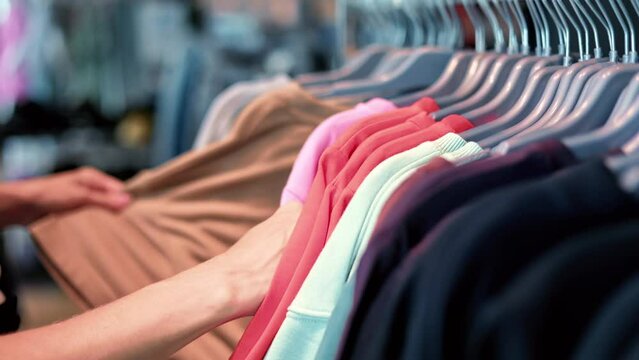 Female hands choosing apparel blouse t shirt hanging on rack at clothes fashion store enjoy shopping