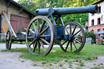 Single massive grey cannon replica on two rusty wheels with base and barrel visible stanting next...