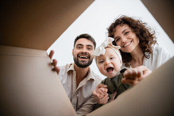 bottom view of happy parents and excited infant girl looking inside of carton box.