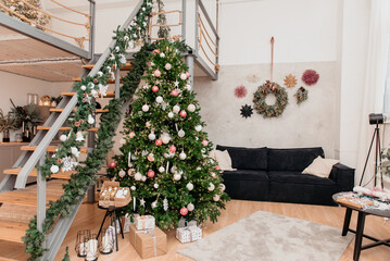 Christmas room in the house with a staircase and a large Christmas tree decorated with New Year's toys