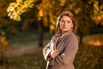 A thoughtful woman in a warm coat against the background of autumn golden leaves. Autumn portrait