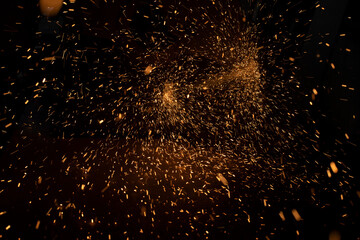 Fototapeta na wymiar Sparks in dark. Lots of bright lights on black background. Burning metal particles fly in different directions.