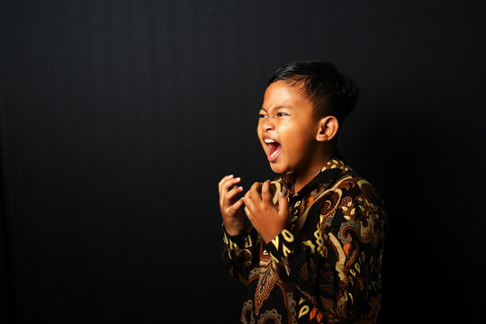 An Asian kid wearing Batik is screaming isolated on black background.