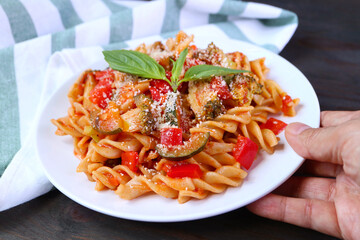 Hand Placing a Plate of Delectable Fusilli Pasta in Marinara Sauce on Wooden Table