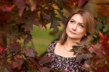 Portrait of a young woman on a background of burgundy leaves in autumn