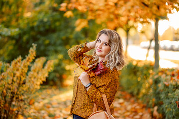 Autumn portrait of a plus- size girl with a bouquet of yellow leaves in her hands . Stylish woman in the autumn park