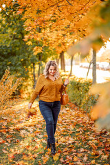 young stylish plus-size woman with a bouquet of yellow leaves walks in an autumn park