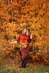 young beautiful plus-size woman stands near an autumn tree.