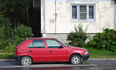 An old red car with a flat tire stands near a residential building, Antonova-Ovseenko Street, St. Petersburg, Russia, September 2022