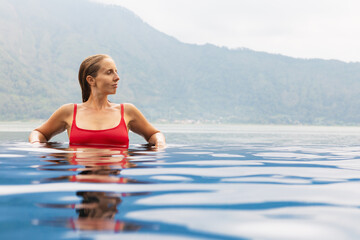 Young woman relax in infinity pool with lake view. Natural hot spring spa under Batur volcano....