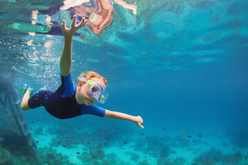 Happy family - active kid in wetsuit and snorkeling mask dive underwater, see tropical fishes in coral reef sea pool. Travel adventure, swimming activity on summer beach vacation with child.